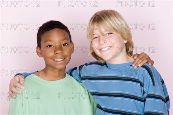 Studio shot portrait of two teenagers with arms around, head and shoulders. Photo : Rob Lewine