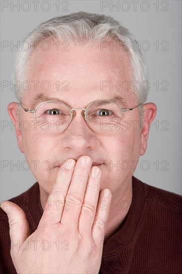 Studio shot portrait of senior man with hand covering mouth, close-up. Photo : Rob Lewine