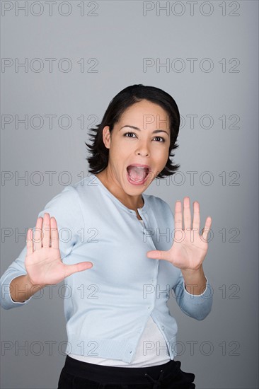 Studio shot portrait of mid adult woman with arms raised and open mouth, waist up. Photo : Rob Lewine