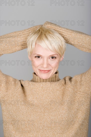 Studio shot portrait of mid adult woman with hands behind head, head and shoulders. Photo : Rob Lewine