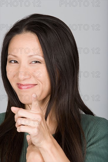 Studio shot portrait of mid adult woman pointing at viewer, head and shoulders. Photo : Rob Lewine