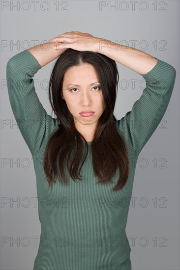 Studio shot portrait of mid adult woman with arms raised, waist up. Photo : Rob Lewine