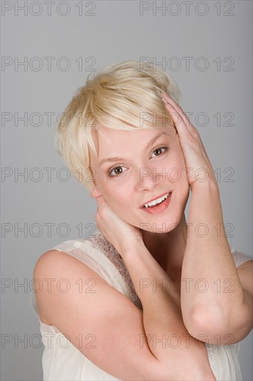 Studio shot portrait of young woman with head in hands, head and shoulders. Photo : Rob Lewine