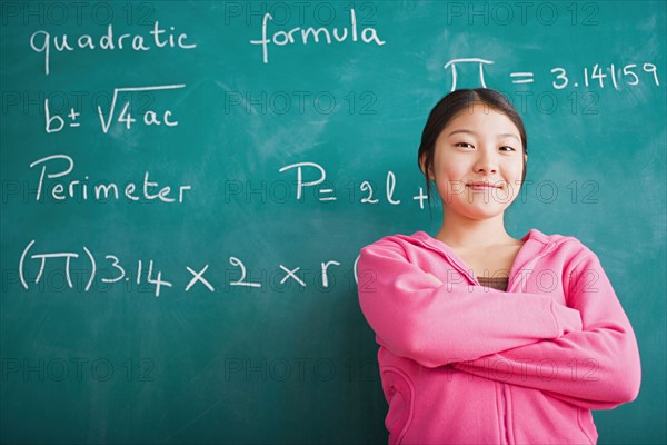 Happy Asian girl standing against blackboard after solving mathematical equation. Photo : Rob Lewine
