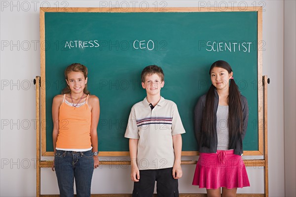 Two schoolgirls and schoolboy standing against blackboard with profession names written above. Photo : Rob Lewine