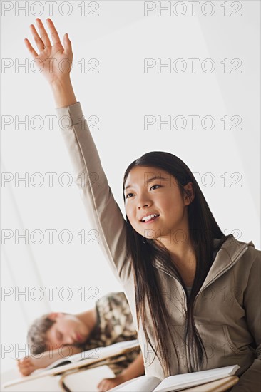 Happy schoolgirl rising hand in classroom while her colleague is sleeping on his desk. Photo : Rob Lewine