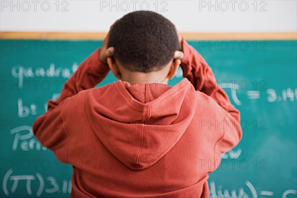 Frustrated schoolboy standing in front of blackboard. Photo : Rob Lewine
