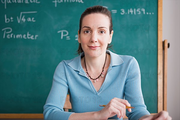 Confident female teacher posing against blackboard. Photo : Rob Lewine