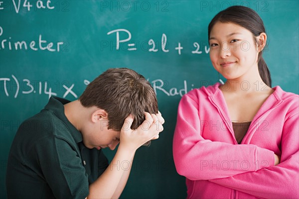 Happy girl and frustrated boy standing in front of blackboard with mathematical formula. Photo : Rob Lewine
