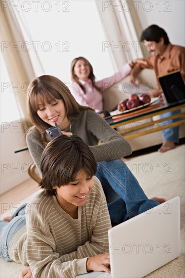 Brother and sister using laptop and mobile, parents in background. Photo : Rob Lewine