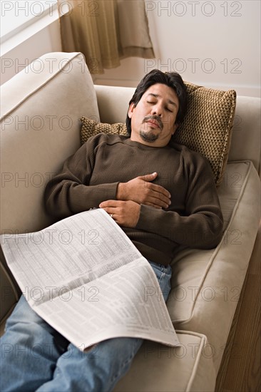 Mature man sleeping on sofa with newspaper. Photo : Rob Lewine