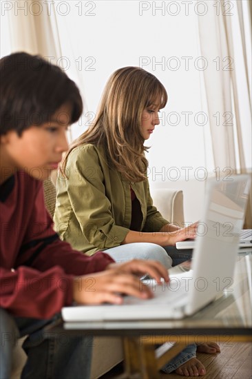 Brother and sister using laptops in living room. Photo : Rob Lewine