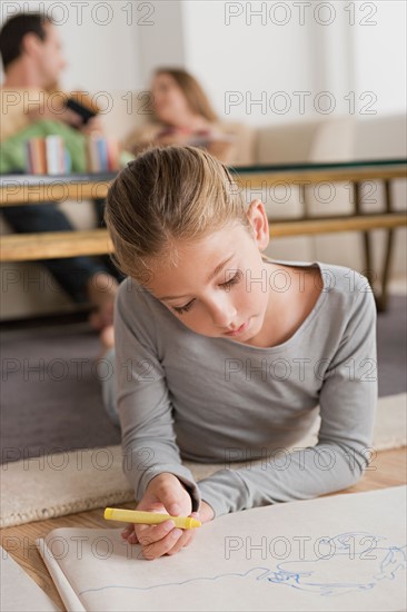 Girl (12-13) drawing in living room, parents in background. Photo : Rob Lewine