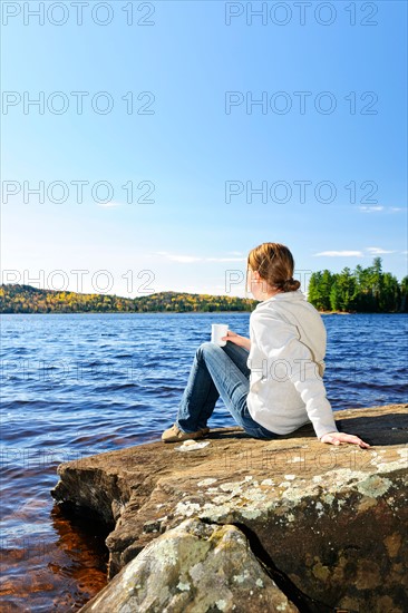 Canada, Ontario, Algonquin Park, Teenage girl sitting on rock and looking at lake. Photo :  Elena Elisseeva
