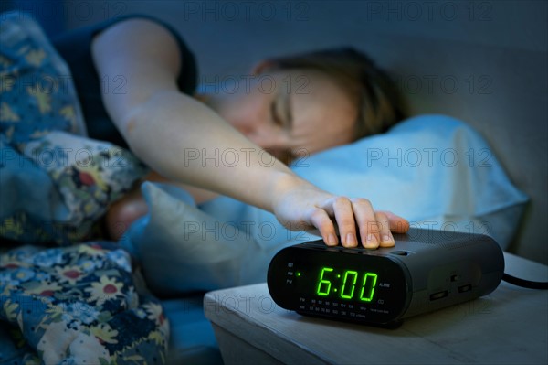 Teenage girl with hand on alarm clock. Photo : Elena Elisseeva