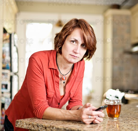 Woman in kitchen with glass of tea and cell phone. Photo : Elena Elisseeva