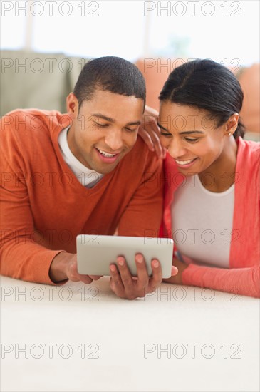 Couple lying on floor reading e-book.