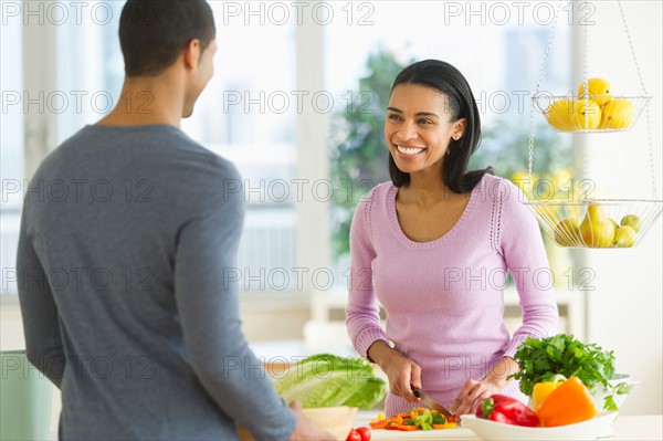 Couple chopping vegetables in kitchen.