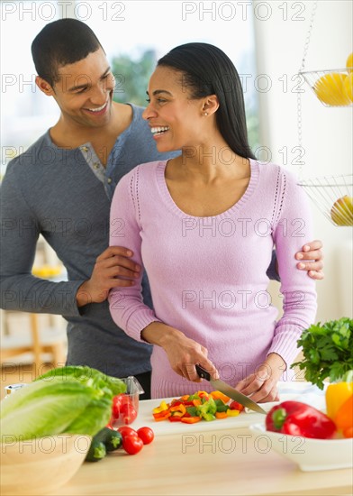 Couple chopping vegetables in kitchen.