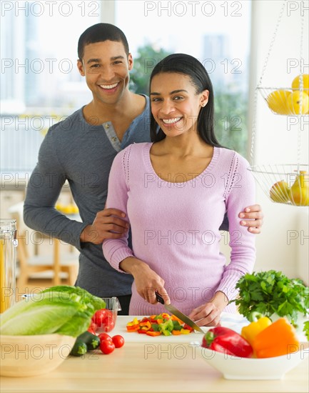 Portrait of couple chopping vegetables in kitchen.