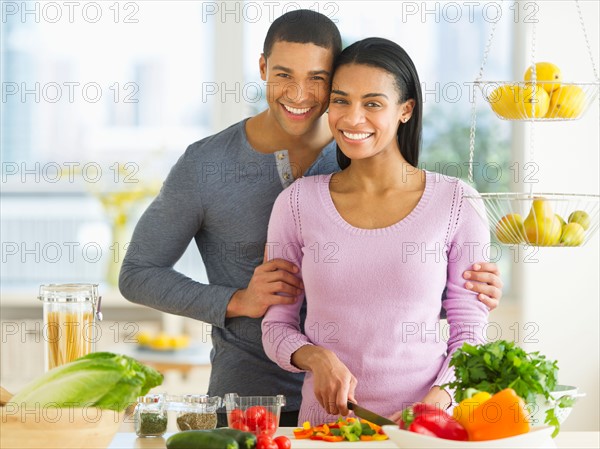 Portrait of couple chopping vegetables in kitchen.