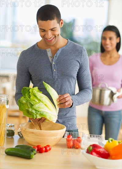 Couple preparing salad in kitchen.