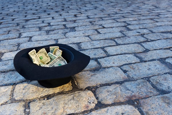 Money in hat on cobblestone street.