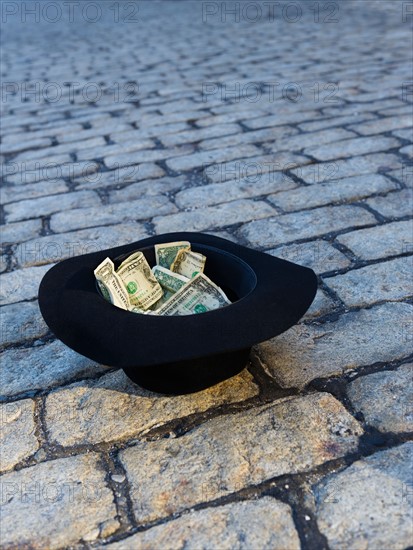 Money in hat on cobblestone street.