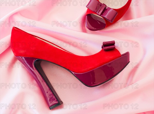Pair of red high heel open toe shoes on pink textile.