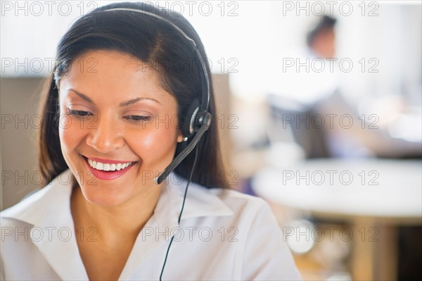 Businesswoman with headset, businessman in background.