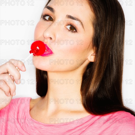 Studio portrait of young woman licking lollypop.