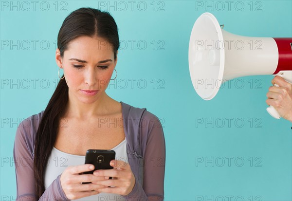 Studio shot of woman texting and ignoring voice from bullhorn.