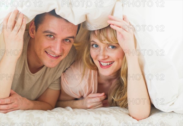 Couple lying on bed under duvet.