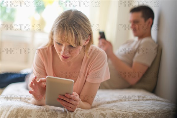 Couple lying on bed and using digital devices.