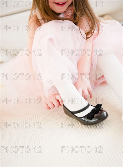 Small girl (4-5 years) in tulle dress putting on shoe. Photo : Jamie Grill