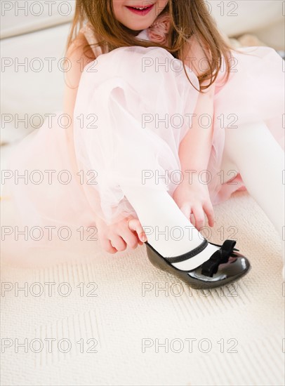 Small girl  (4-5 years)  in tulle dress putting on shoe. Photo : Jamie Grill