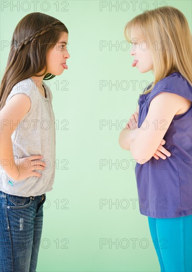 Two girls standing face to face and sticking out tongues. Photo : Jamie Grill