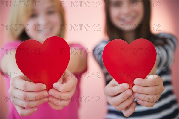 Close up of two girl's hands holding red hearts. Photo : Jamie Grill