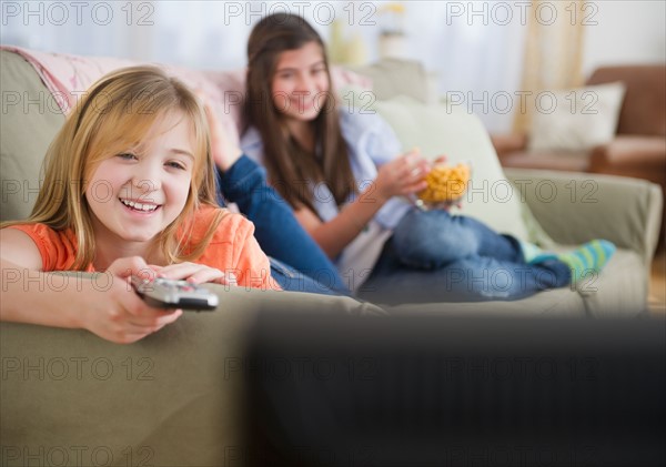 Two girls watching tv on sofa. Photo : Jamie Grill