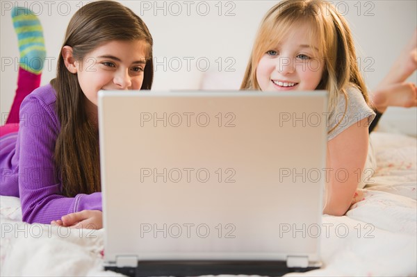 Two girls using laptop on bed. Photo : Jamie Grill