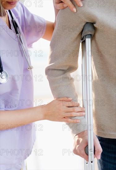 Close up of female doctor helping patient with crutch. Photo : Jamie Grill