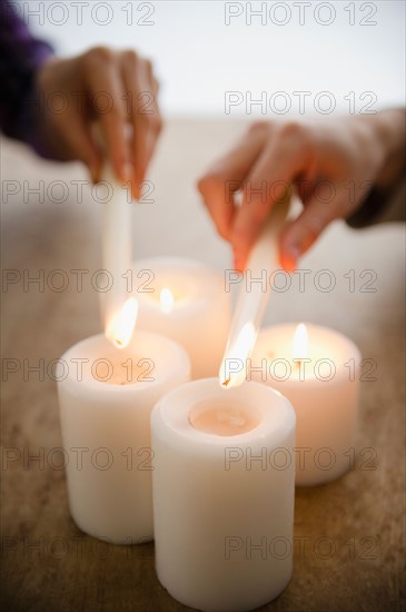Close up of man's and woman's hands igniting candles. Photo : Jamie Grill