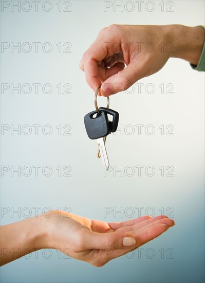 Close up of man's and woman's hands with car key, studio shot. Photo : Jamie Grill