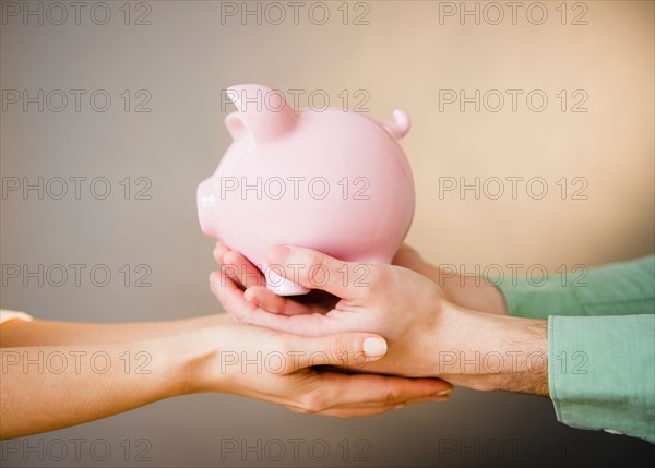 Close up of man's and woman's hands holding piggy bank, studio shot. Photo : Jamie Grill