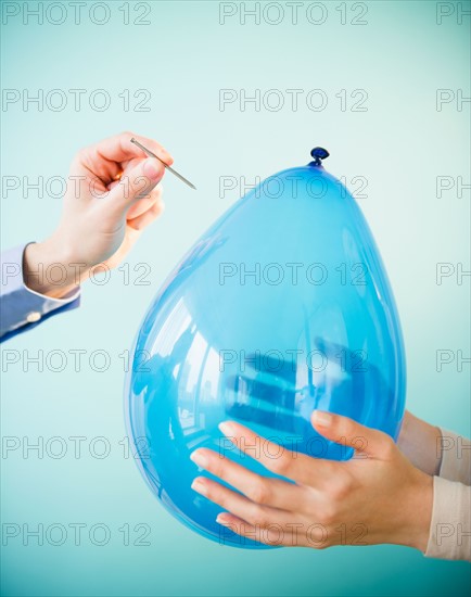 Close up of man's and woman's handholding balloon and nail,  studio shot. Photo : Jamie Grill