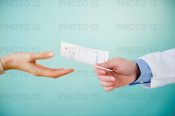 Close up of doctor's hand giving prescription to patient,  studio shot. Photo : Jamie Grill