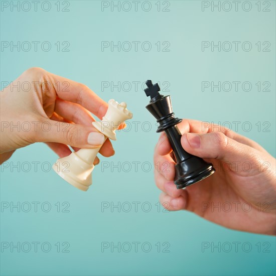 Close up of man's and woman's hands holding chess pieces,  studio shot. Photo : Jamie Grill