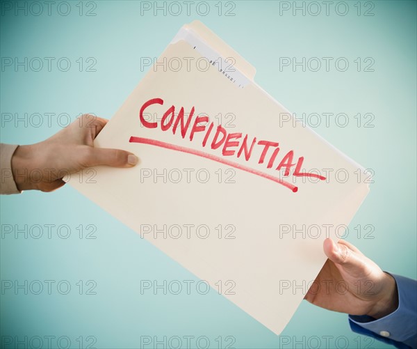 Close up of man's and woman's hands holding confidential document, studio shot. Photo : Jamie Grill