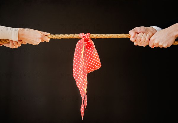 Close up of man's and woman's hands pulling rope, studio shot. Photo : Jamie Grill