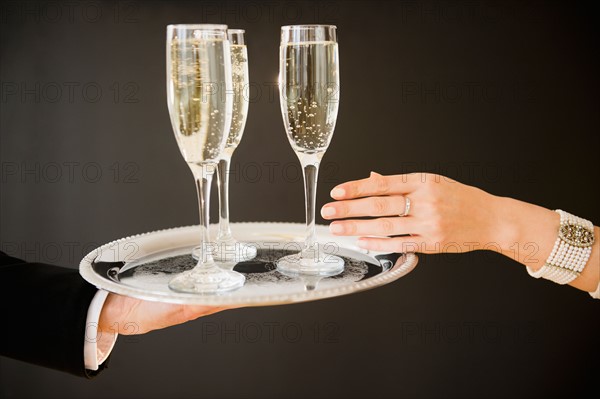Close up of man's and woman's hands and tray with champagne flutes, studio shot. Photo : Jamie Grill